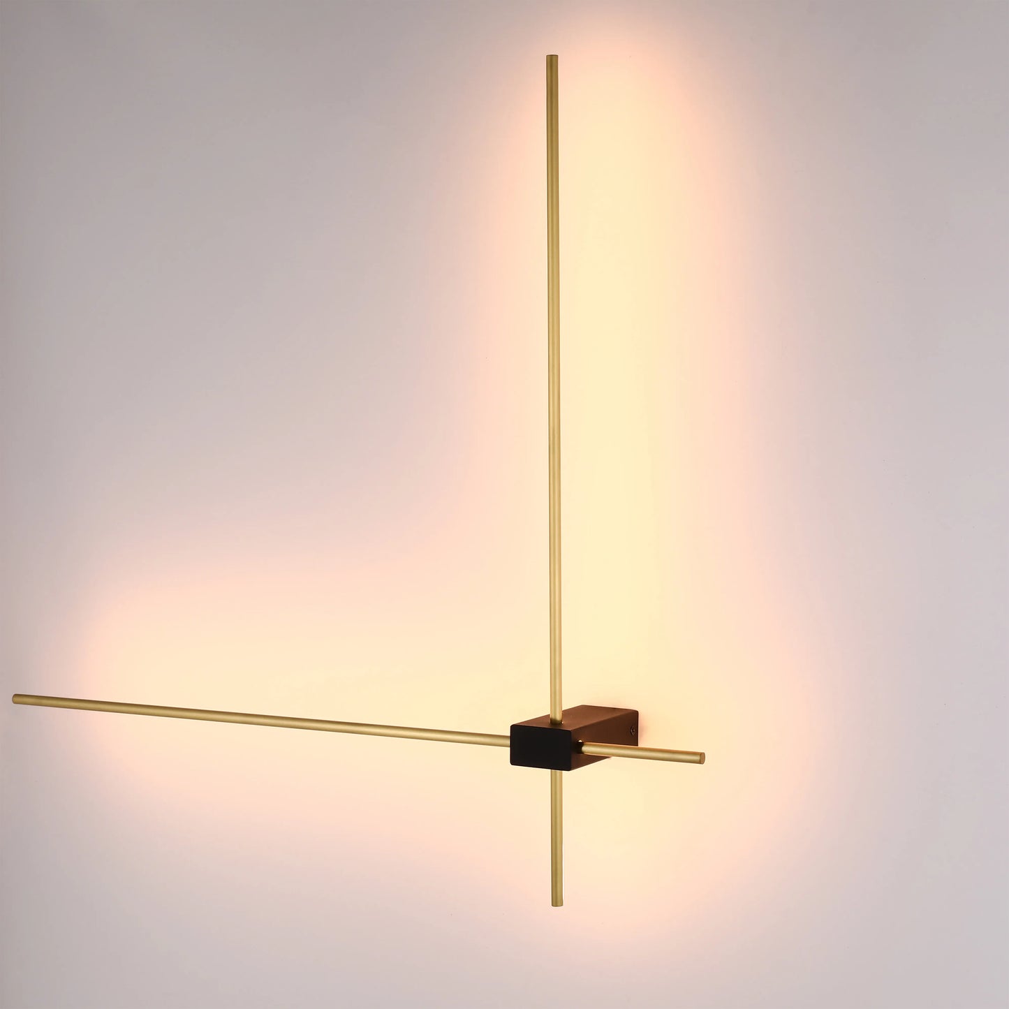 Stylish wall-mounted light with gold bars and a black cube, casting a warm glow on the wall.
