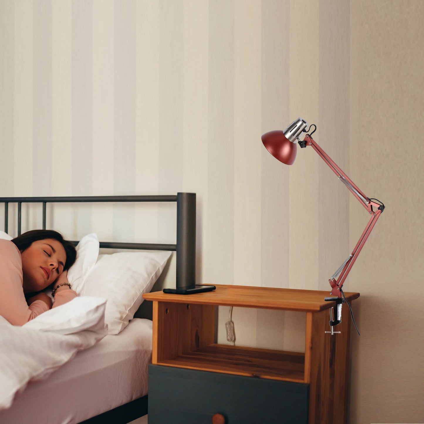 An adjustable red desk lamp is clipped to a bedside table, providing focused illumination to the scene.