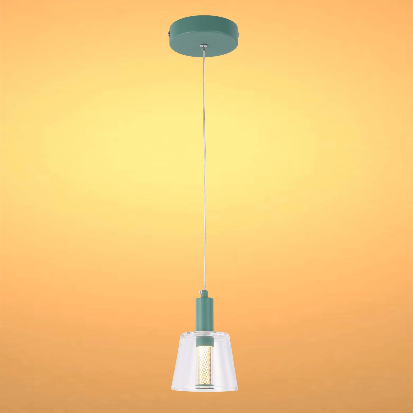 A hanging pendant light with a clear glass shade and a green mount against an orange background.