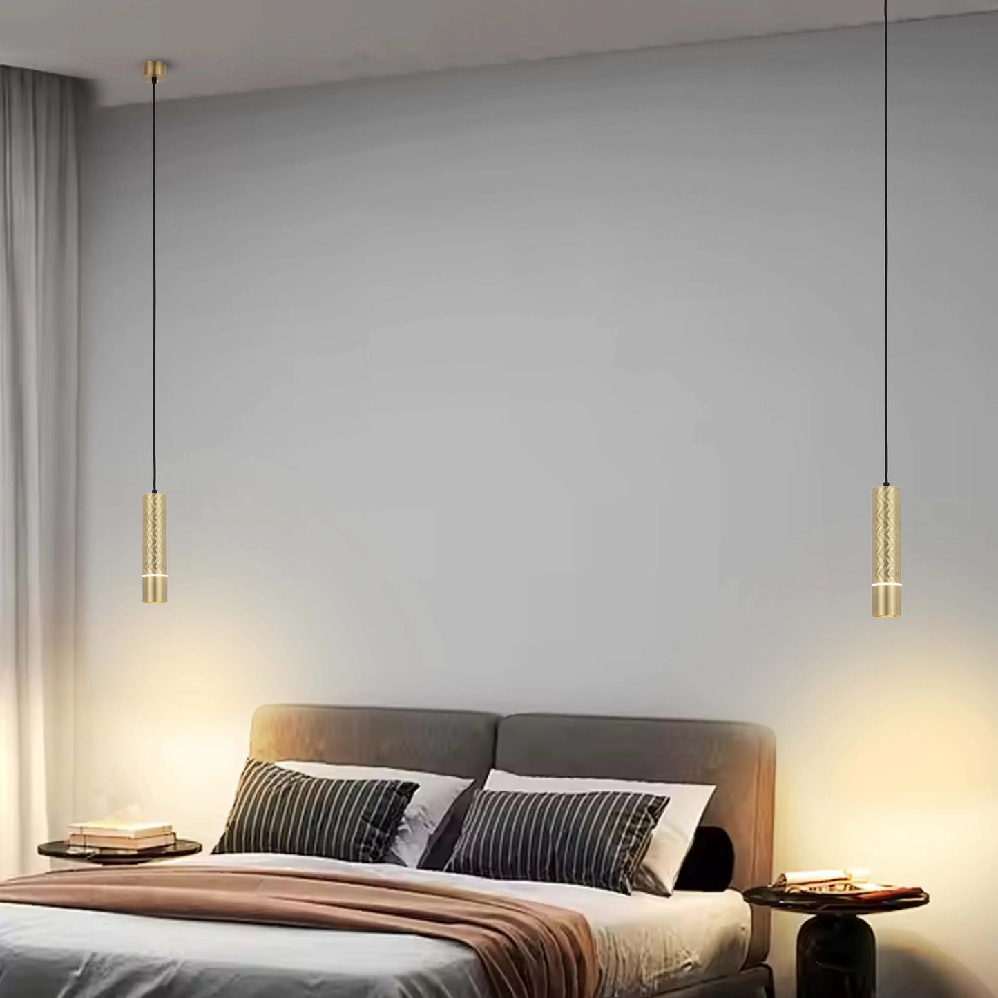 Two gold, pendant lights either side of a double bed, illuminating the bedside tables. Modern bedroom lighting.
