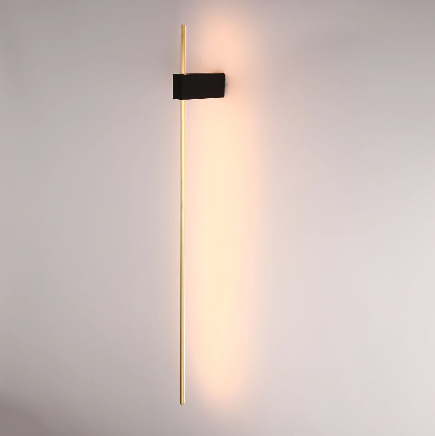 Sleek, modern wall light with a long gold bar and a black rectangular mount, casting a warm glow onto the wall.