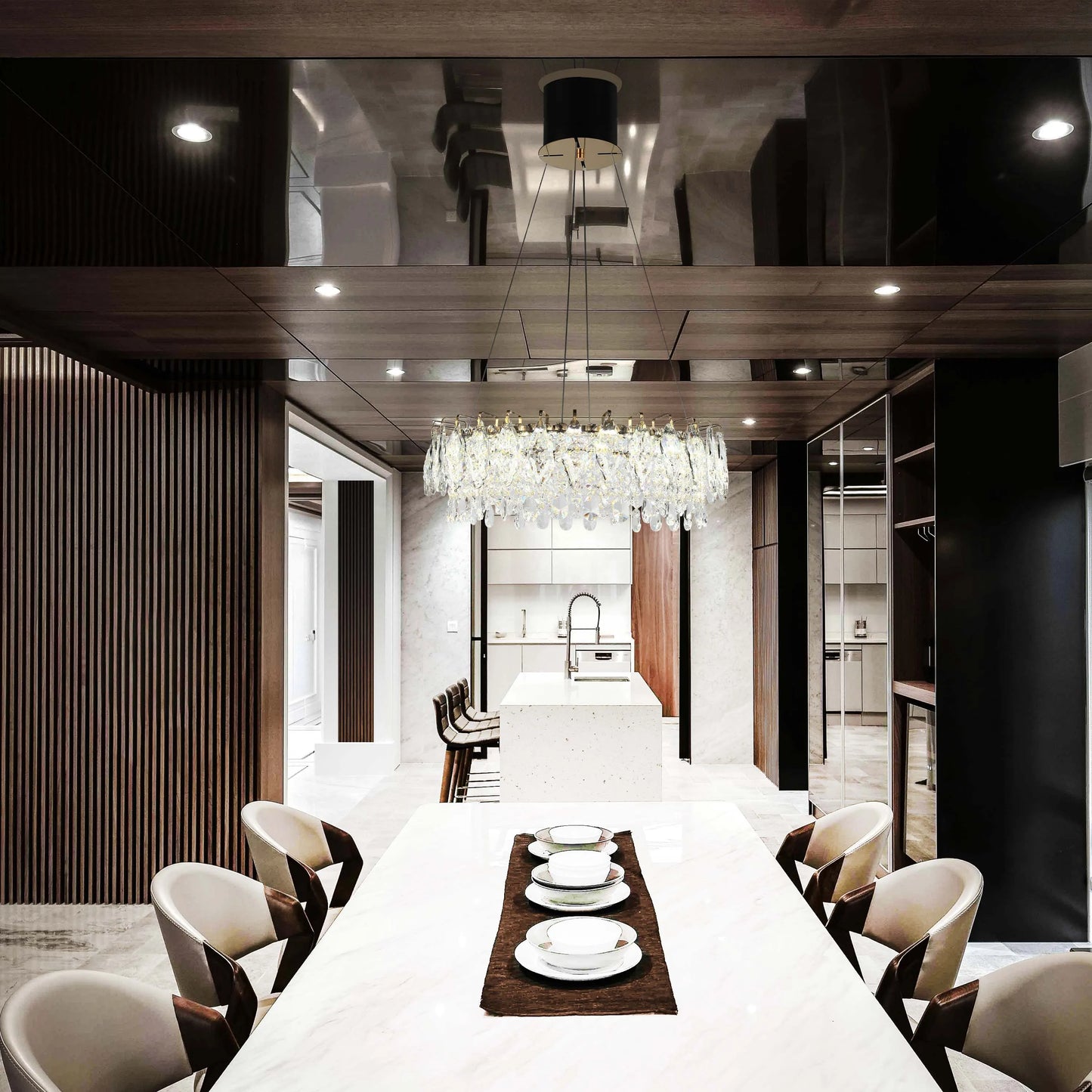 A modern dining room boasts a crystal chandelier above a marble table, complemented by subtle recessed lighting in a glossy ceiling.