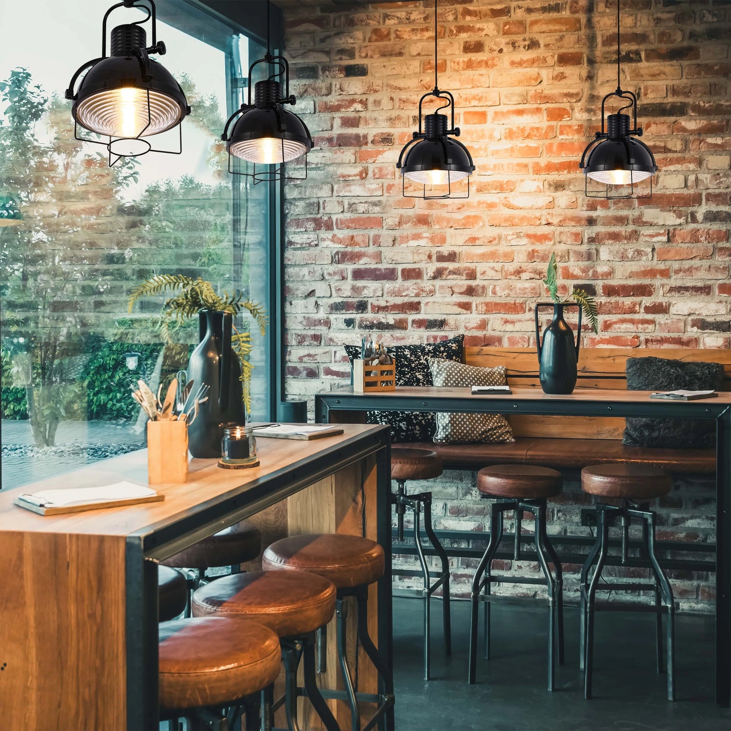 A row of four black, industrial style pendant lights hang over a high table with stools in a modern kitchen with exposed brickwork.