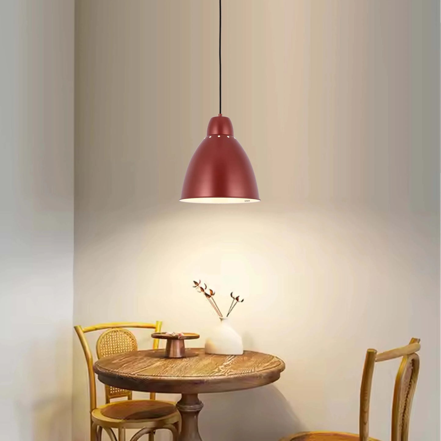 A burgundy pendant light illuminates a round wooden table with two chairs in a warmly lit room, creating an inviting atmosphere.