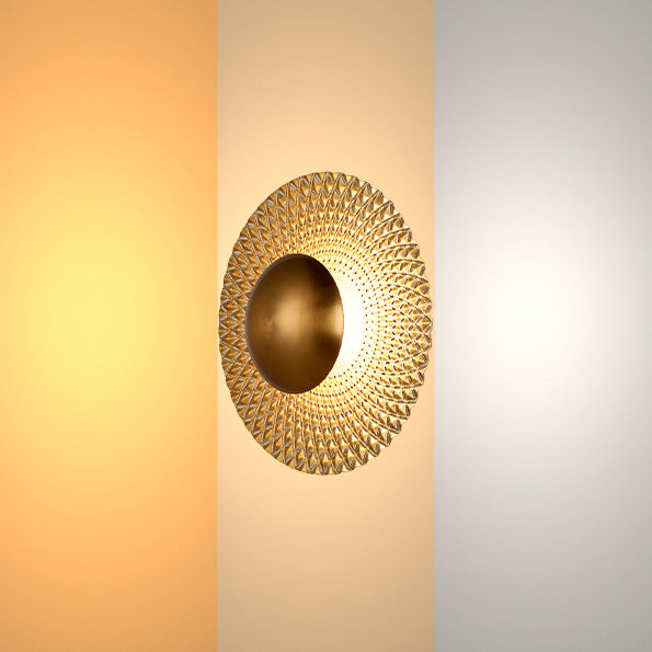 A gold wall light with a round, textured shade, evenly lit with a soft, diffused glow.