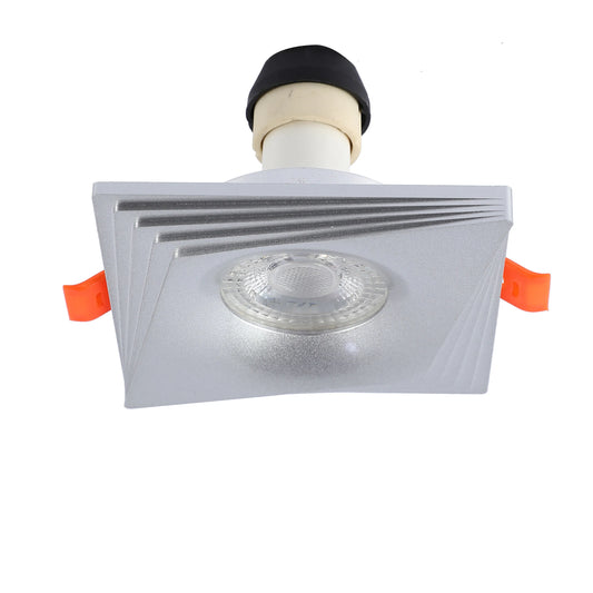 Square silver downlight with a refractive lens, emitting bright, even light. Has orange spring clips for easy installation.