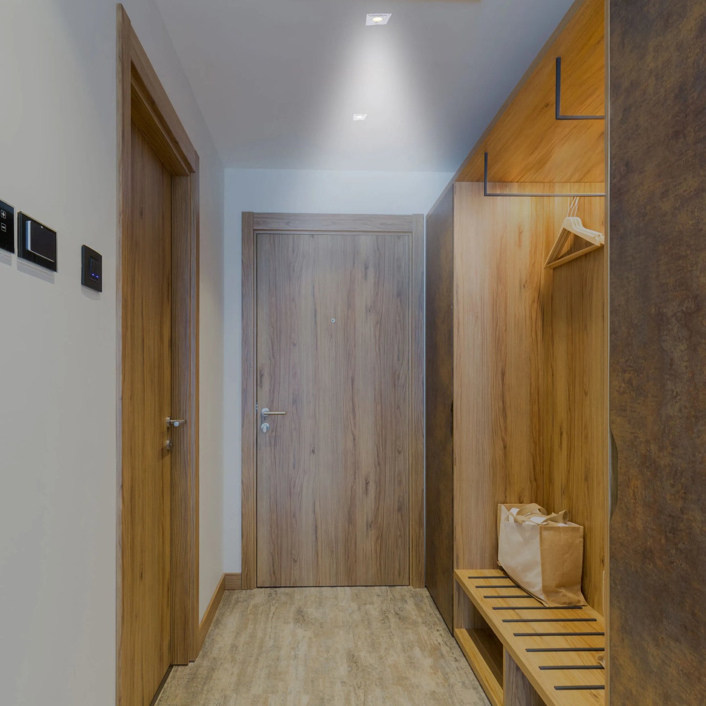 Recessed downlights provide a wash of light, illuminating the modern hallway with fitted wardrobe and light wood doors.
