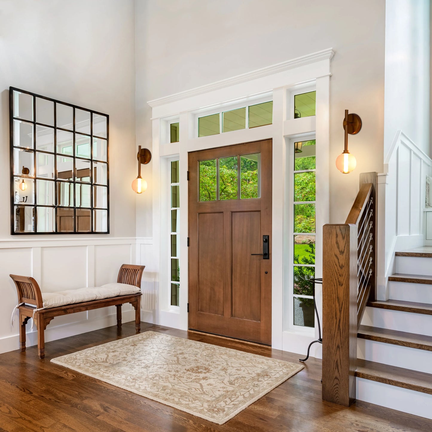 Wall lights frame the doorway and mirror, providing a soft, ambient glow in this bright and airy entryway.