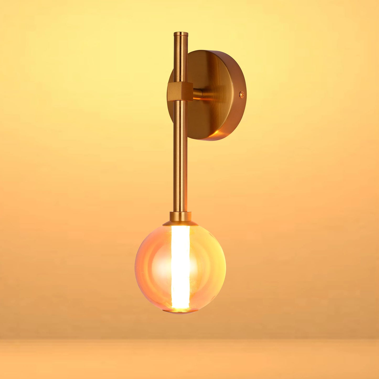 A modern wall light with a brass finish and a spherical glass shade, emitting a warm, ambient glow.