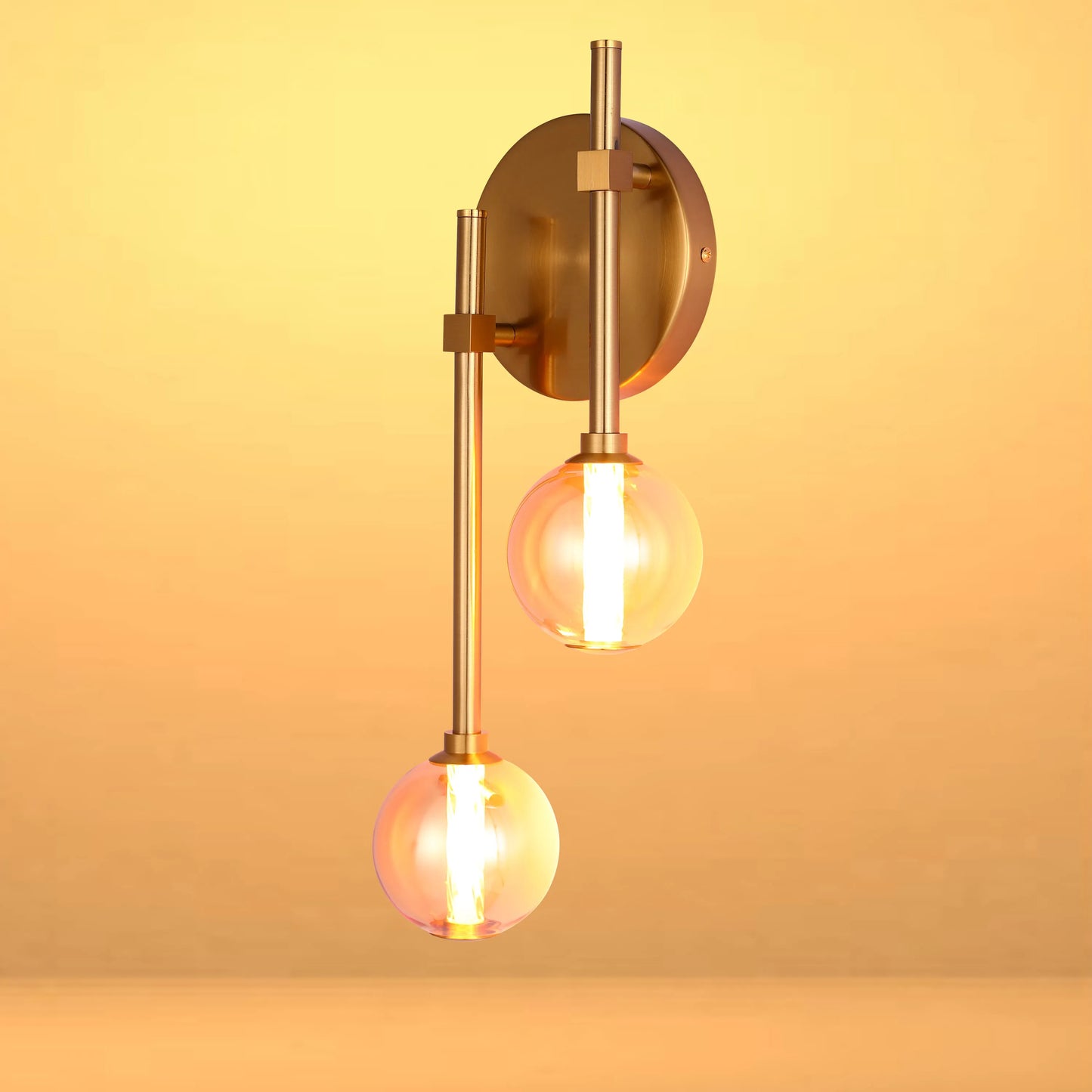 Gold wall light with two illuminated spherical bulbs against a yellow gradient background.