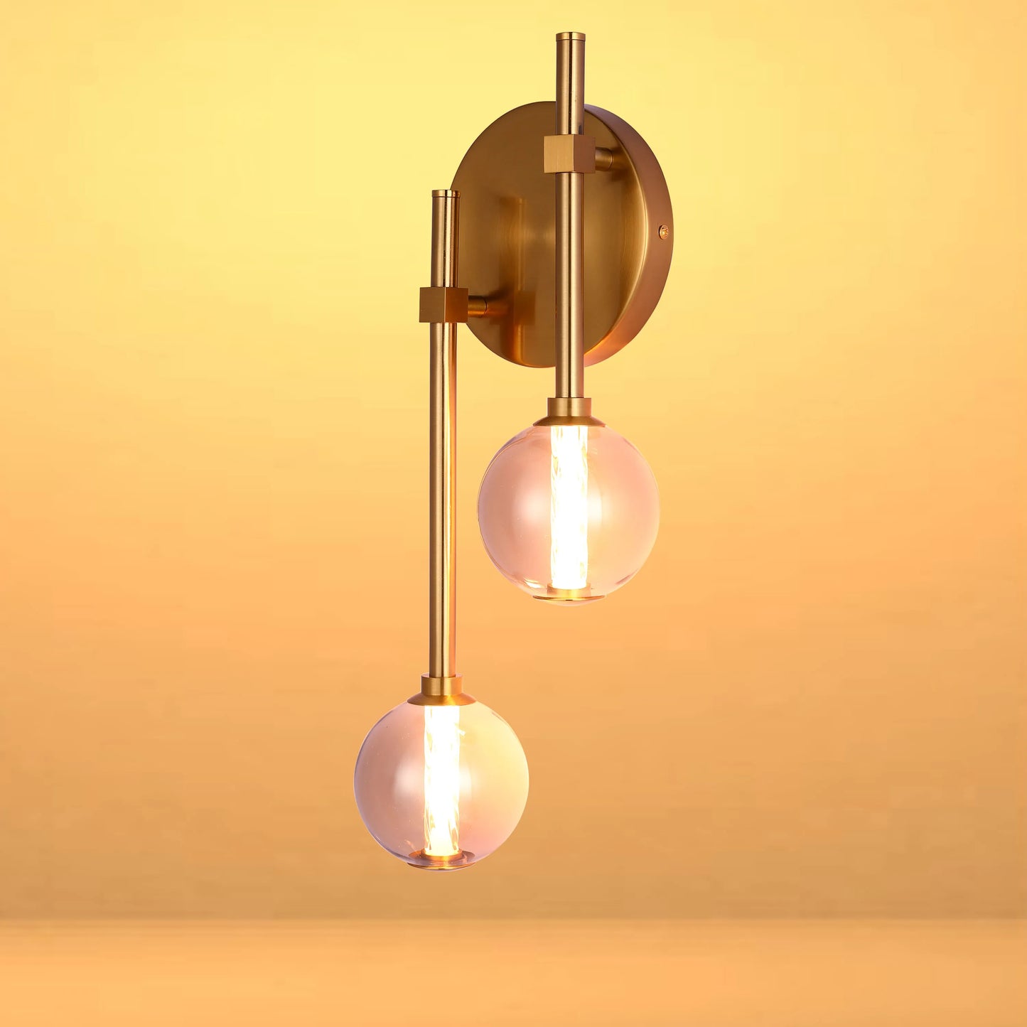 Contemporary brass wall light with two illuminated glass globe shades, casting a warm glow.