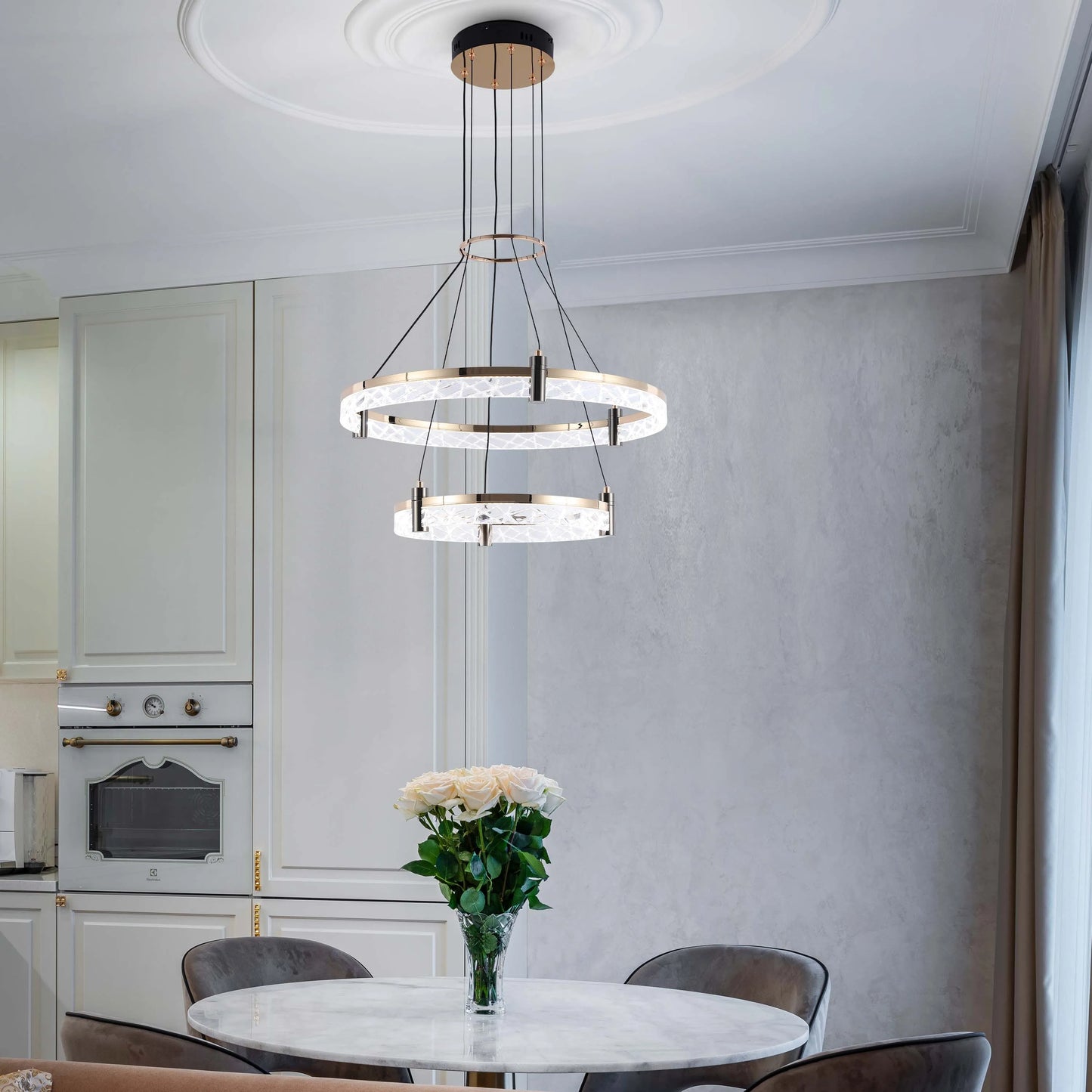 A luxurious two-tiered circular chandelier hangs above a marble dining table in a modern, elegant kitchen.