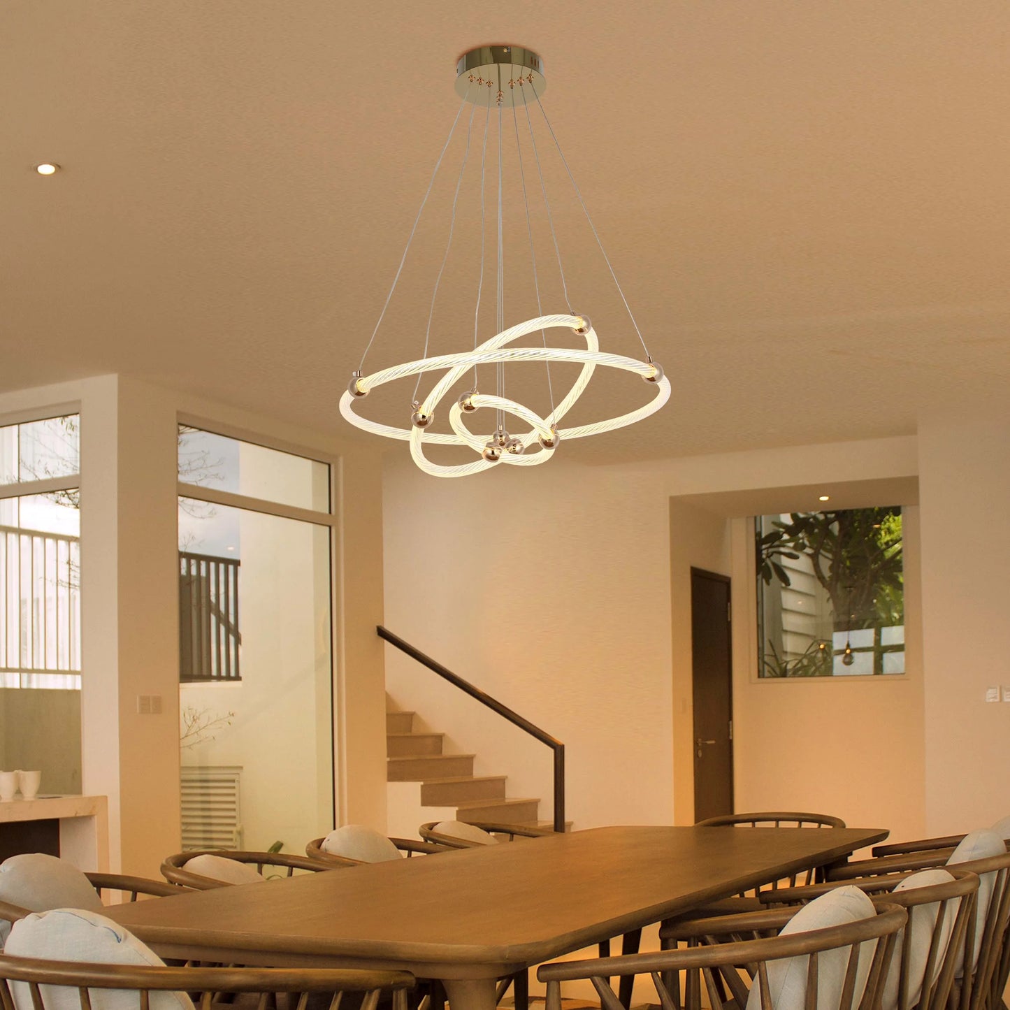A modern chandelier with ring-shaped lights and reflective spherical accents hangs above a wooden dining table.