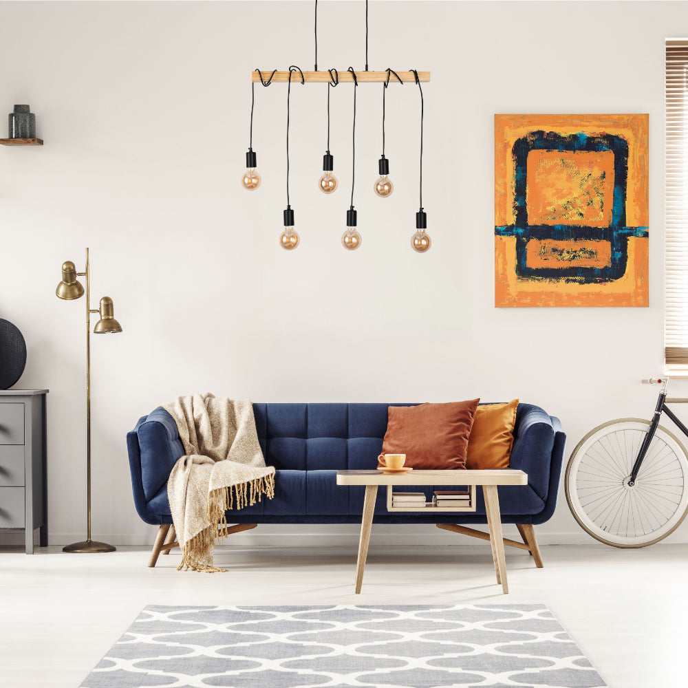 Stylish lighting fixture with exposed bulbs hangs above a plush, navy sofa, creating a warm, inviting atmosphere.