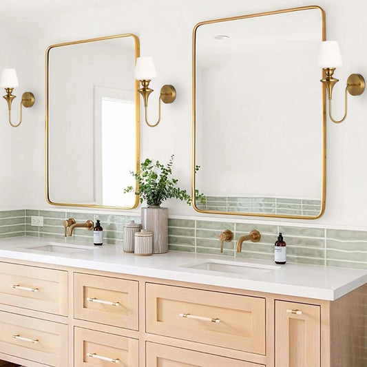 Two brass wall sconces with white shades illuminate the bathroom vanity and framed mirrors.