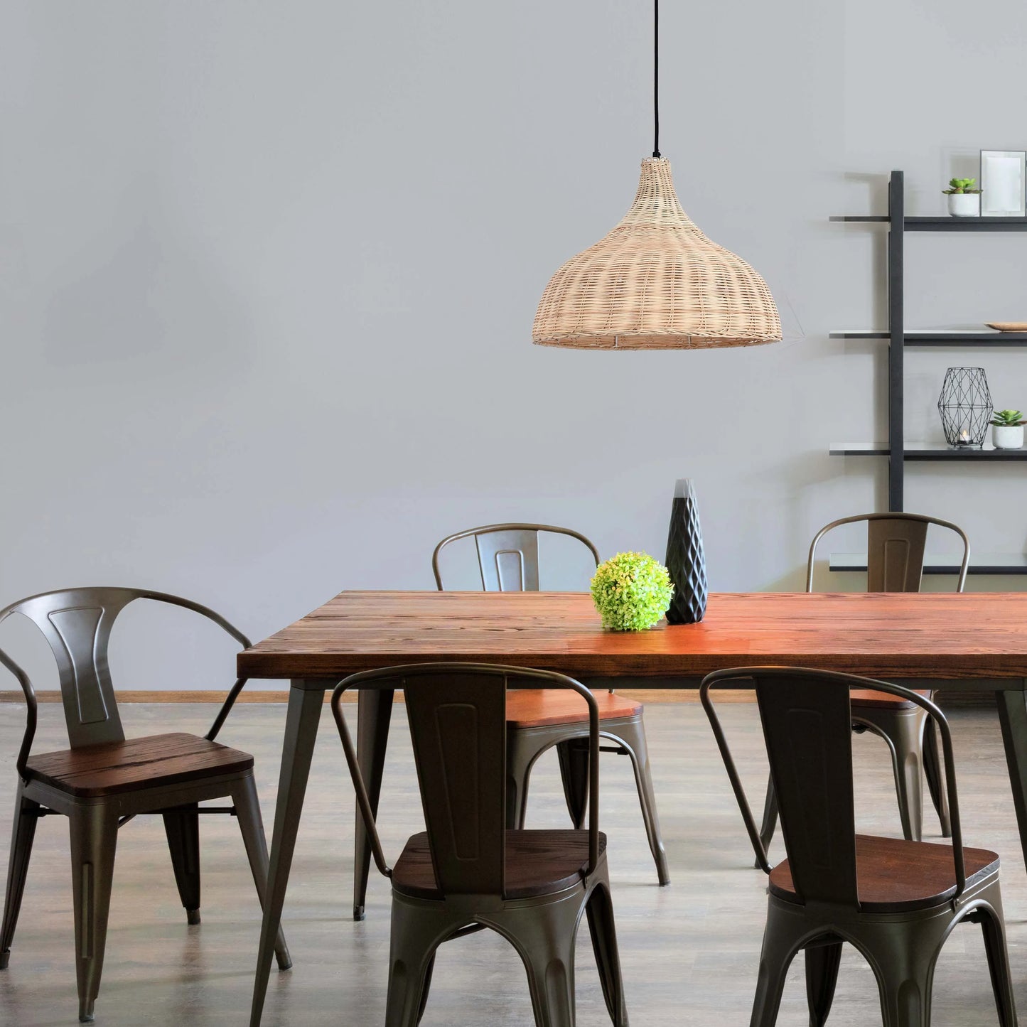 A woven pendant light hangs above a wooden dining table with rustic metal chairs. Natural light illuminates the room, casting a soft glow.