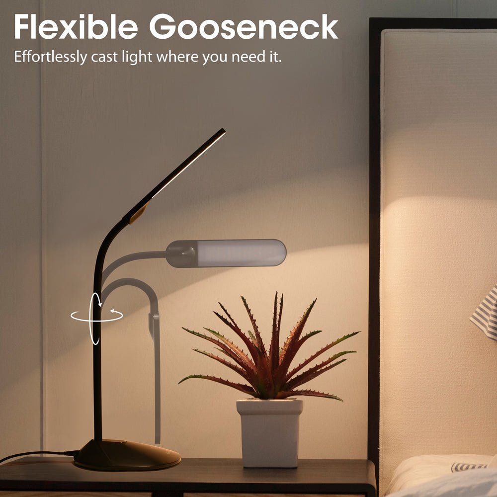 A modern bedside table lamp with a gooseneck design next to a potted plant, sitting on a stylish bedside table.