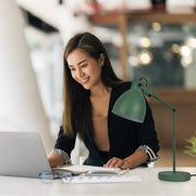 A green adjustable desk lamp casts a focused glow, complementing a modern office space.