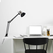 A black adjustable lamp illuminates a minimalist white desk, with a laptop, notebook, and stationery, creating a bright workspace.
