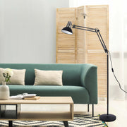 A black articulated floor lamp illuminates a modern living room with a green sofa and wooden coffee table.