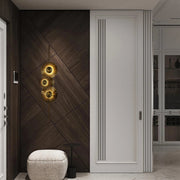 Striking wall-mounted lighting fixture featuring three circular, sunburst-style lamps with a warm, golden glow. A focal point on a dark wood panelled wall.