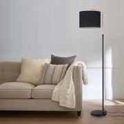 A modern black and gold floor lamp illuminates a beige sofa with cushions. A stylish lighting choice for a living room.
