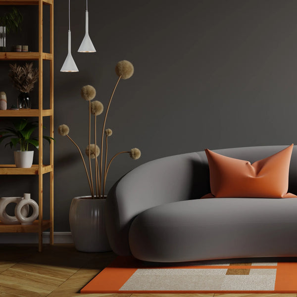Two pendant lights with downward-pointing shades illuminate a sleek grey sofa and a shelf with decorative items.