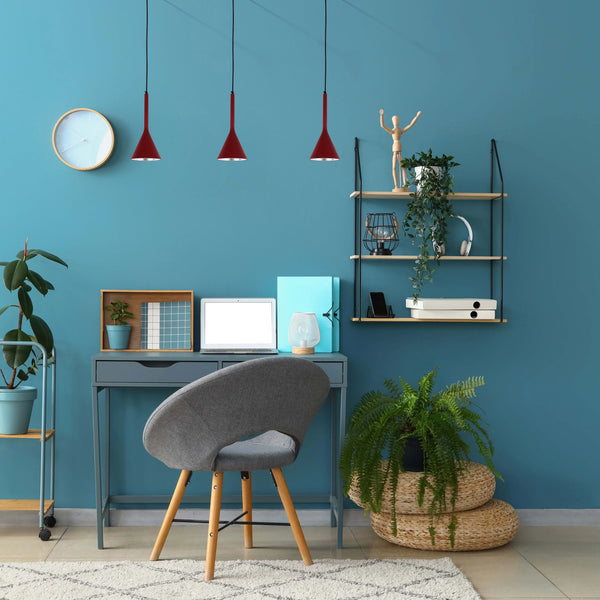 Three red pendant lights hang above a teal-walled office space, creating a modern and stylish working environment with bright illumination.