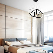 A modern black and white chandelier hangs above a bed in this bright bedroom. Circular rings and cylindrical lights feature.