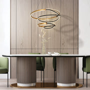 A modern, halo-style pendant light with gold and black rings, above a stylish dining table, provides ambient illumination.