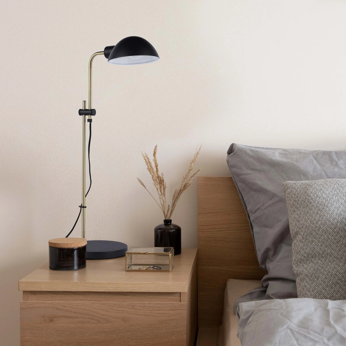Bedside lamp with black shade and gold stand provides warm light, complemented by neutral tones for a cosy atmosphere.