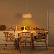 A lit wicker pendant lamp casts a warm glow over a dining table with woven chairs, creating an inviting, rustic atmosphere.