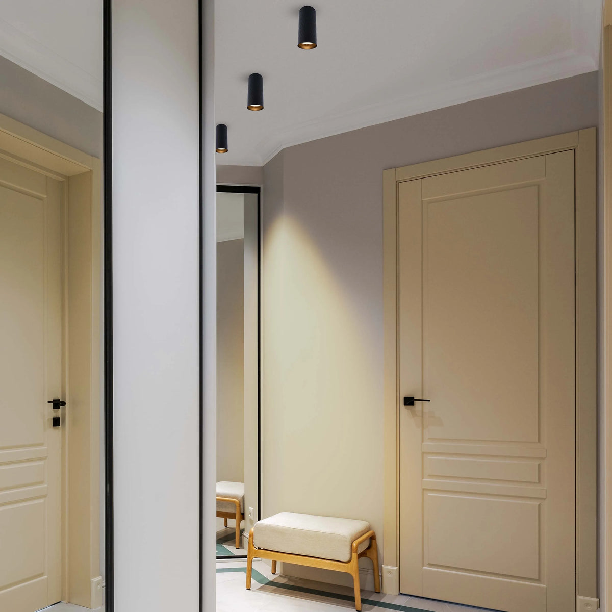 Contemporary black cylinder downlights provide focused pools of light in this hallway, complementing the neutral decor.