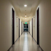 Recessed ceiling lights illuminate a long corridor with doors lining each side, and an exit sign at the end.