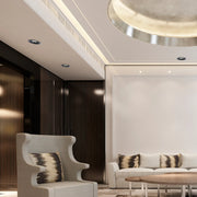 The room features recessed downlights and concealed strip lighting, plus a striking circular ceiling light, creating a warm, layered ambience.