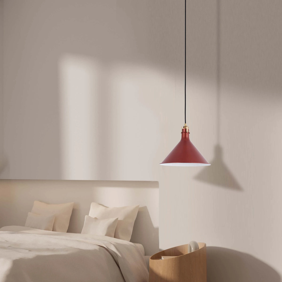 A stylish red pendant light with a white interior hangs over a neutral-toned bedroom setup, casting a soft shadow on the wall.