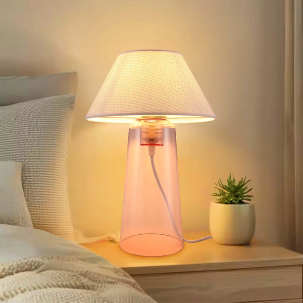 A bedside lamp with a fabric shade and a pink translucent base casts a warm glow onto a wooden bedside table.