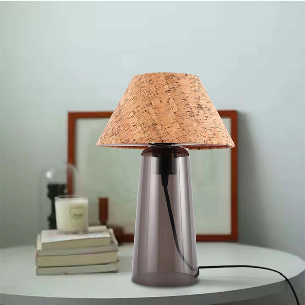 A contemporary table lamp with a cork lampshade and smoked glass base sits on a white side table.