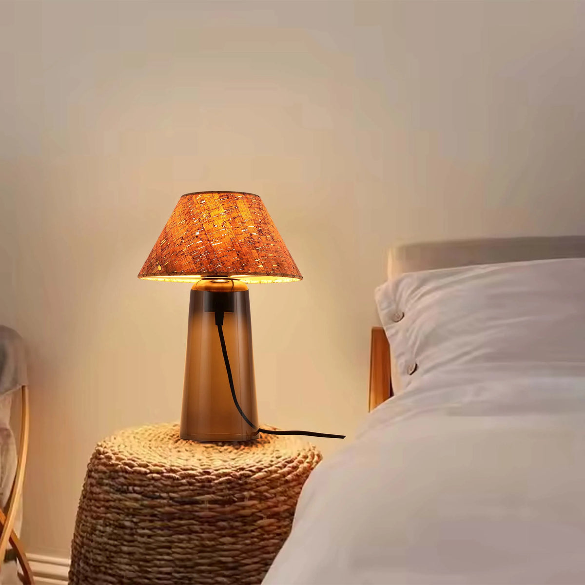 Warm, ambient light from a bedside table lamp with a textured shade creates a cosy atmosphere in a bedroom setting.
