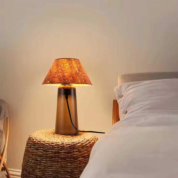 Warm, ambient light from a bedside table lamp with a textured shade creates a cosy atmosphere in a bedroom setting.