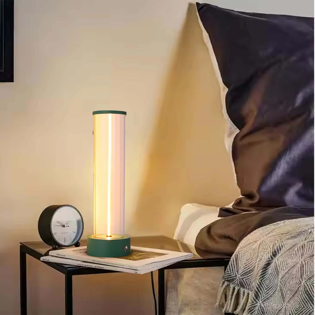 A stylish bedside table lamp emits a soft, vertical glow, complemented by a nearby clock and cosy bedding, creating a warm atmosphere.