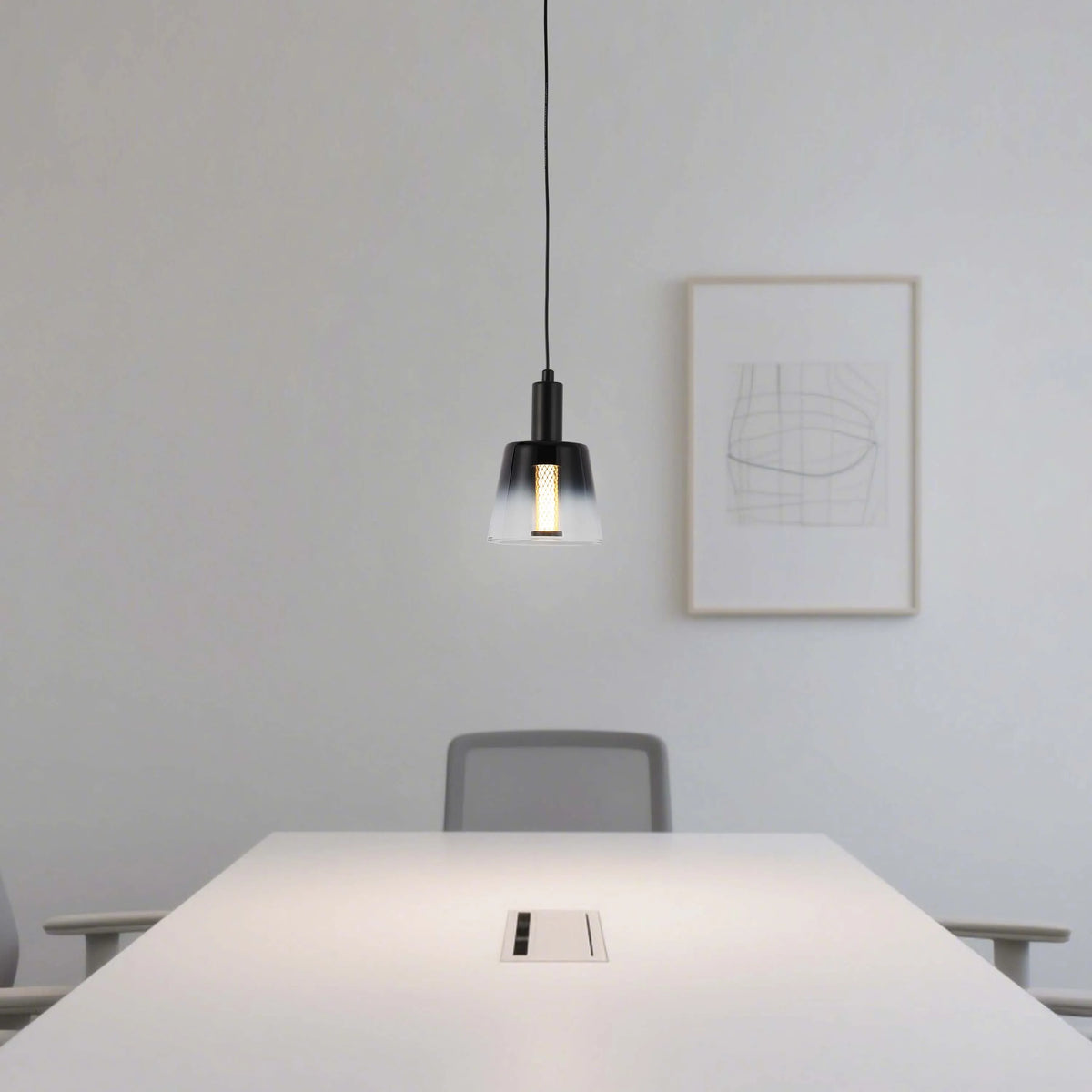 A single pendant light hangs above a conference table, casting a warm glow in a modern, minimalist office space.