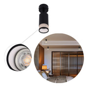 A black ceiling spotlight illuminates a modern bedroom with warm lighting from additional spotlights and a bedside lamp.