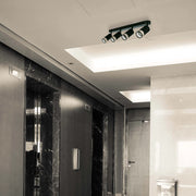 A modern, four-bulb track light fixture with cylindrical lamps provides focused illumination in an interior space.