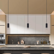 Three black pendant lights hang above a kitchen island, providing focused illumination. The fixtures complement the modern kitchen design.