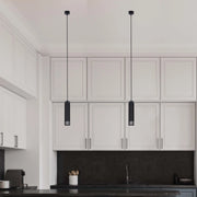 Two pendant lights with black cylindrical shades hang above a modern kitchen island, adding a touch of elegance and focused illumination.