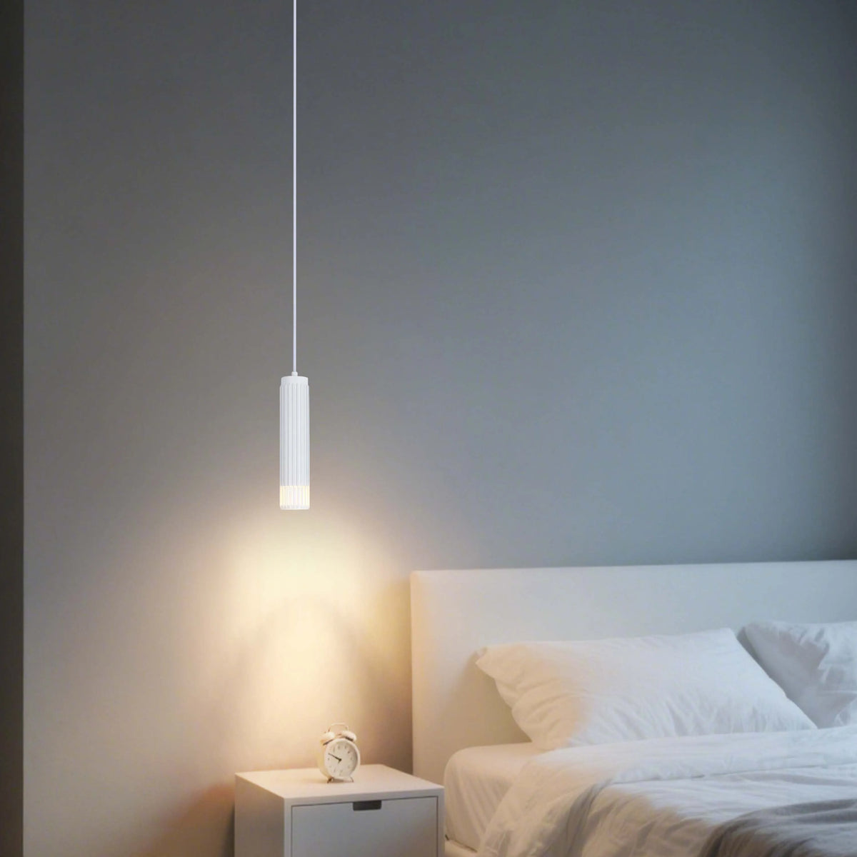 A modern bedroom features a sleek, white pendant light illuminating a bedside table, casting a warm glow in the room.