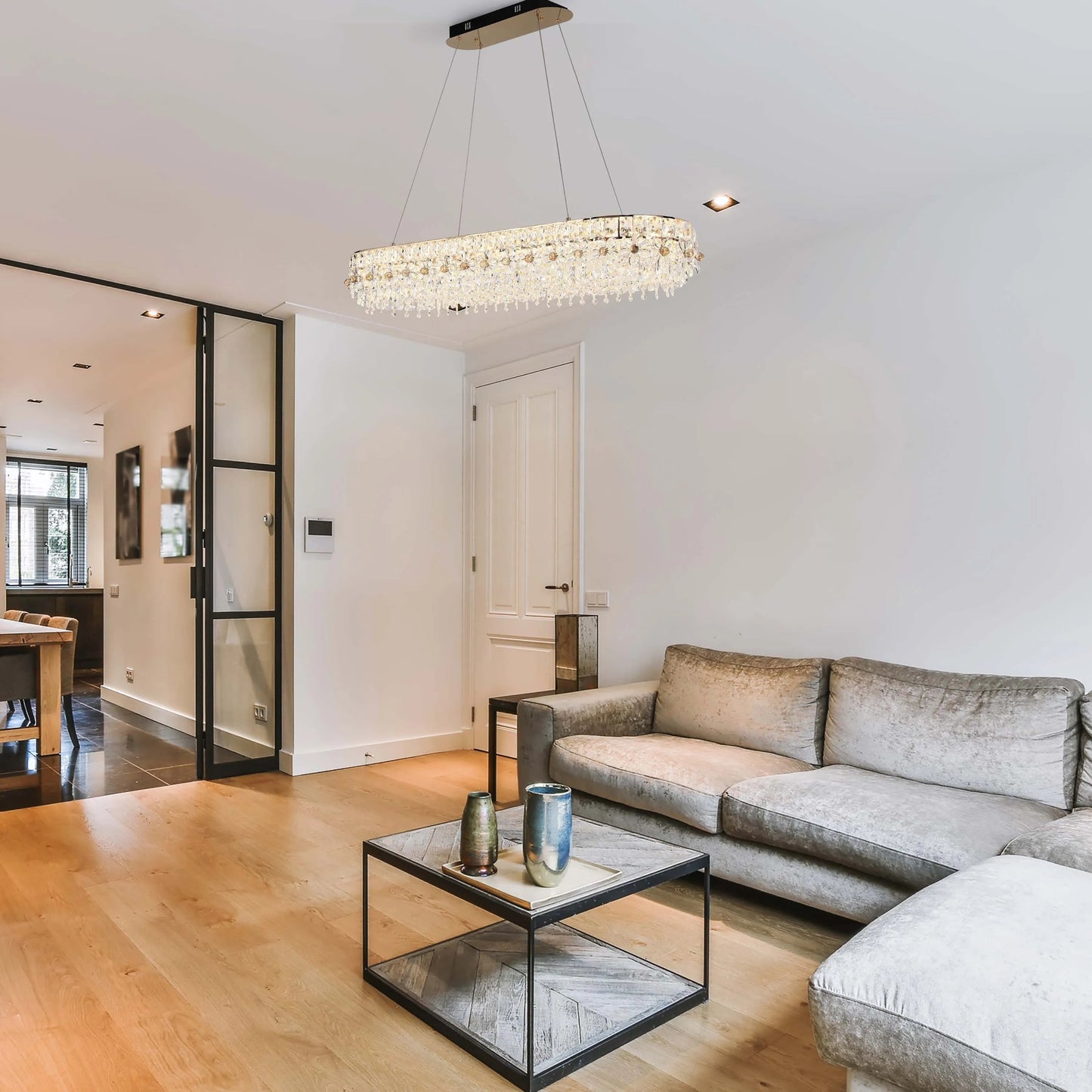 A stylish, glittering crystal chandelier, suspended over a living room area, provides a bright and luxurious focal point.