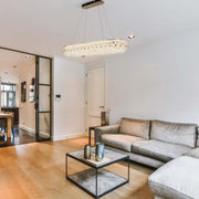 A stylish, glittering crystal chandelier, suspended over a living room area, provides a bright and luxurious focal point.