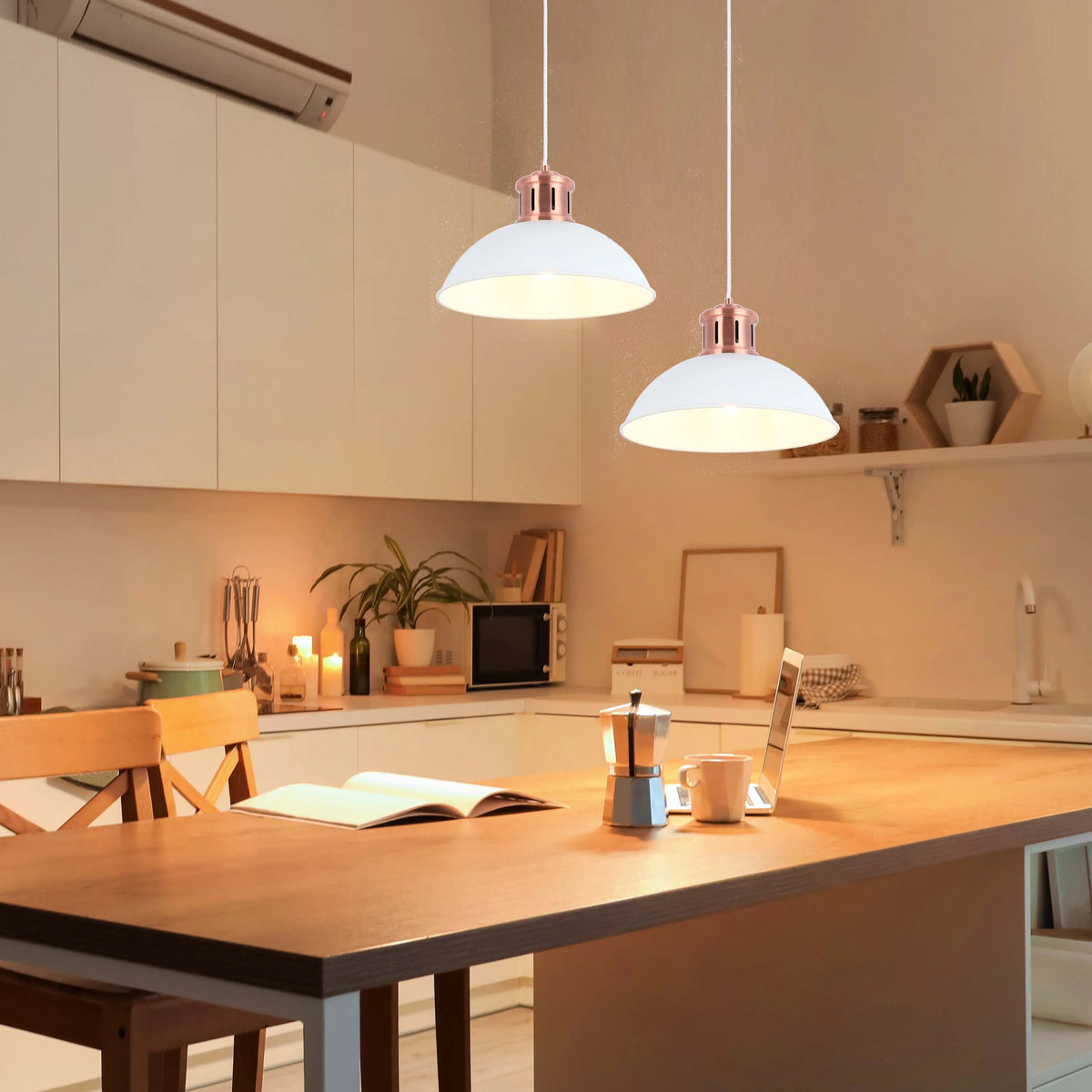 Two pendant lights hang over a kitchen island, casting a warm glow. The shades are white with rose gold accents.